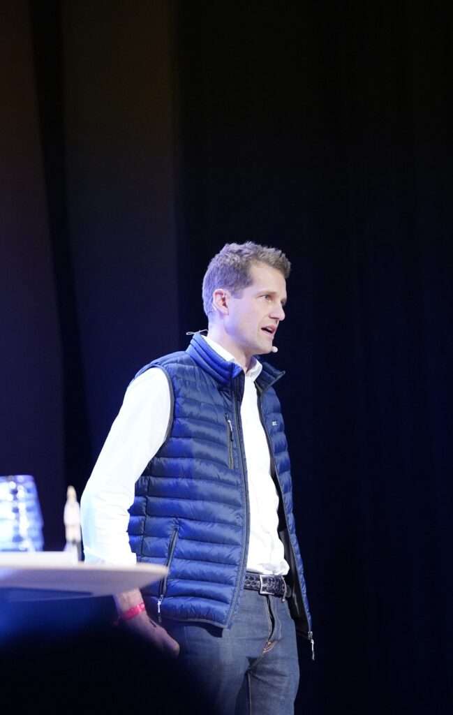 Man in blue vest speaking on stage at a corporate event in Helsinki