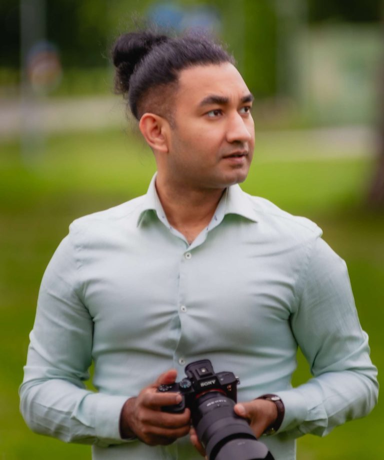 A photographer in Helsinki, specializing in corporate event photography and professional headshots, is holding a camera in the park and looking away.